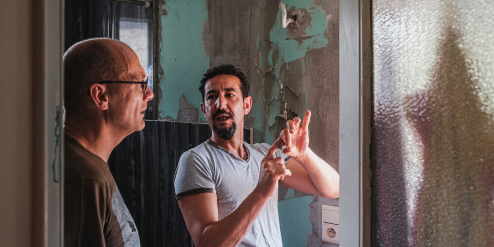 Twee mensen bij een woning in slechte staat.